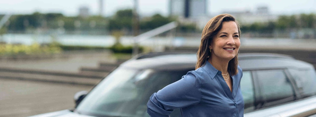 Frau lehnt an einem Gelaender Hintergrund zeigt ein weisses MINI Auto.