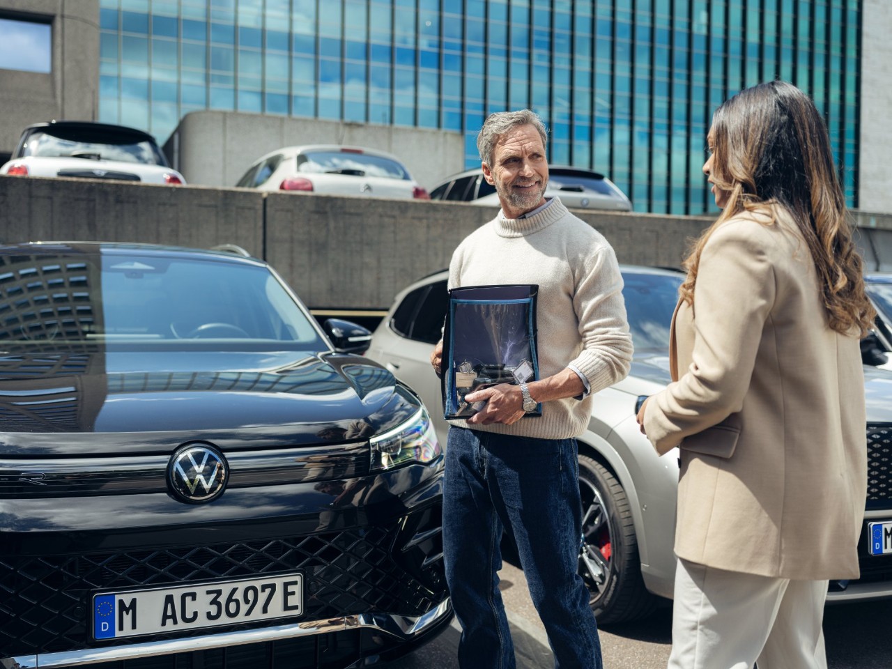 Two people stand next to a Volkswagen.