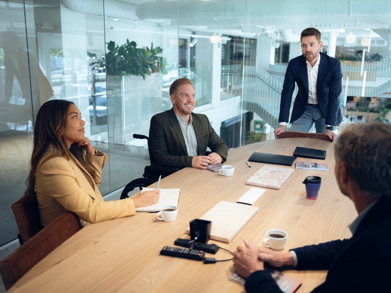 People having a discussion at a wooden table in a modern office with plants and a staircase in the background.