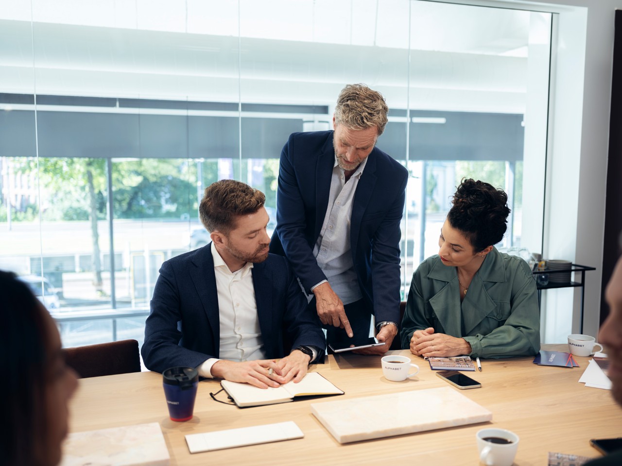 Man shows content on a tablet to two people in a modern office.