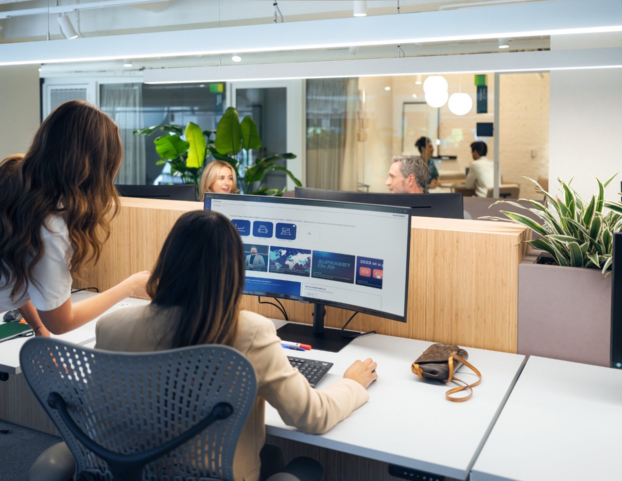 Two women look at a curved monitor in a modern office environment.