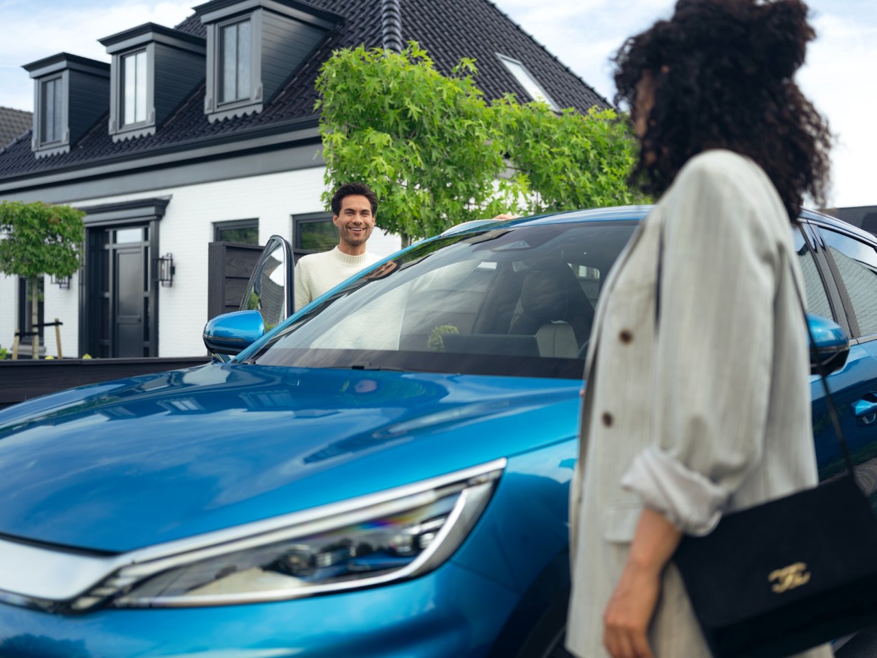  Blue car parked in front of a modern house with two people nearby.