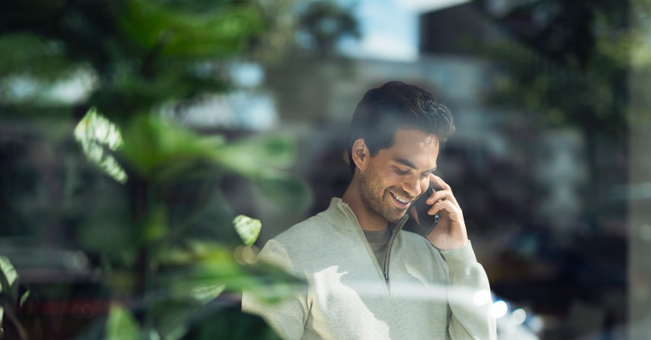 Man talking on a smartphone behind a glass pane.